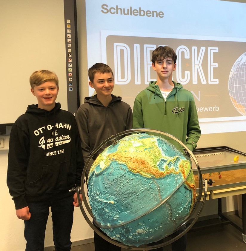 Drei stolze Schüler stehen im Geographie-Raum vor dem Globus