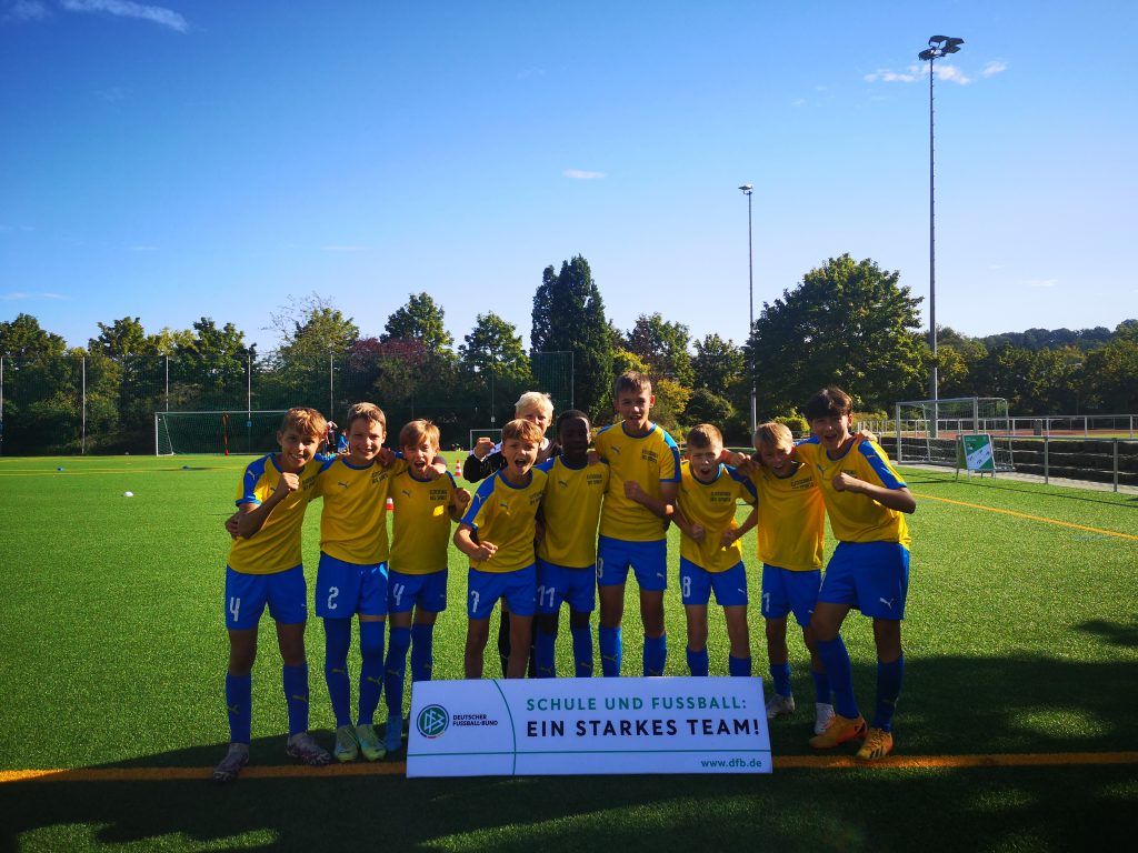 Die DFB Schulcup Mannschaft des OHG in gelben Trikots und blauen Hosen auf dem Rasen eines Sportplatzes.