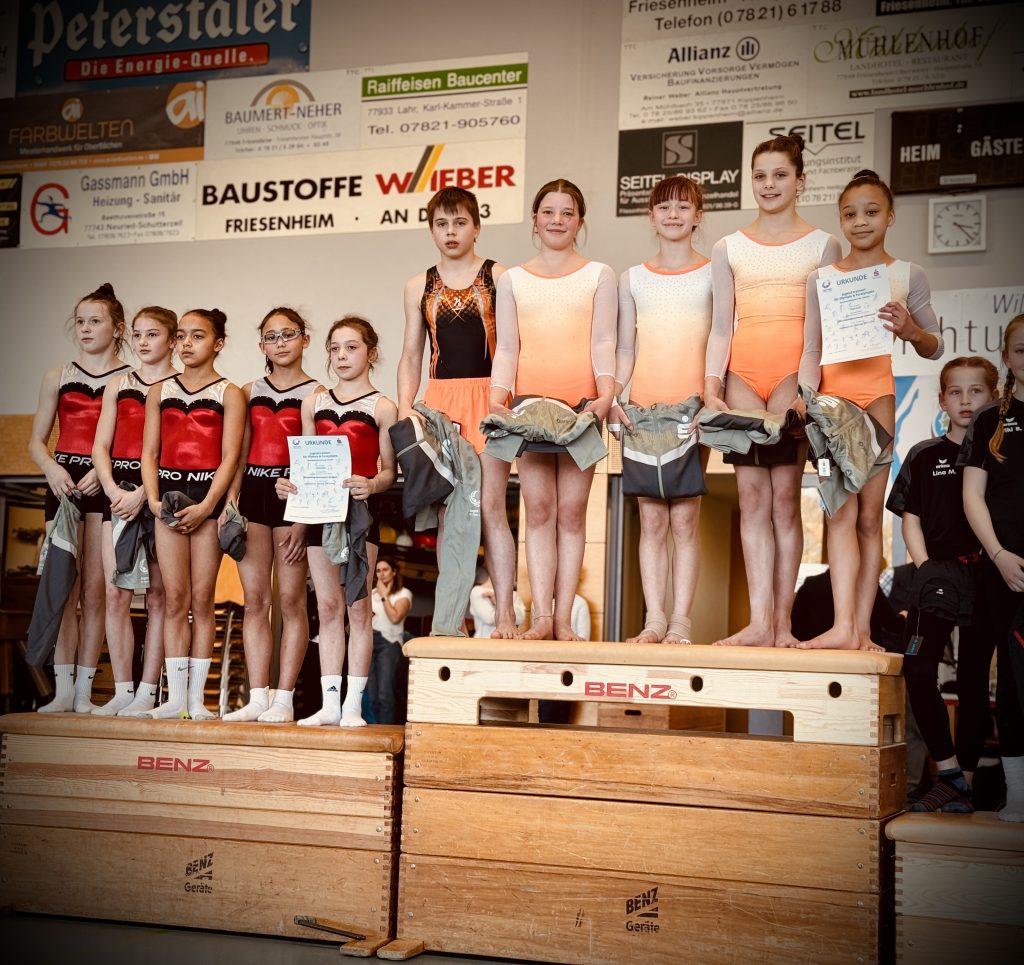 Eine Reihe von stolzen jungen Sportlern mit Urkunden stehen auf Kästen