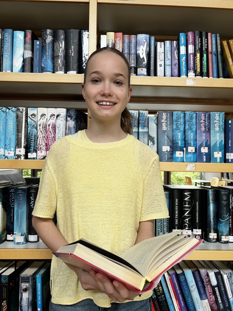 Nina vor dem Bücherregal mit einem Buch in der Hand
